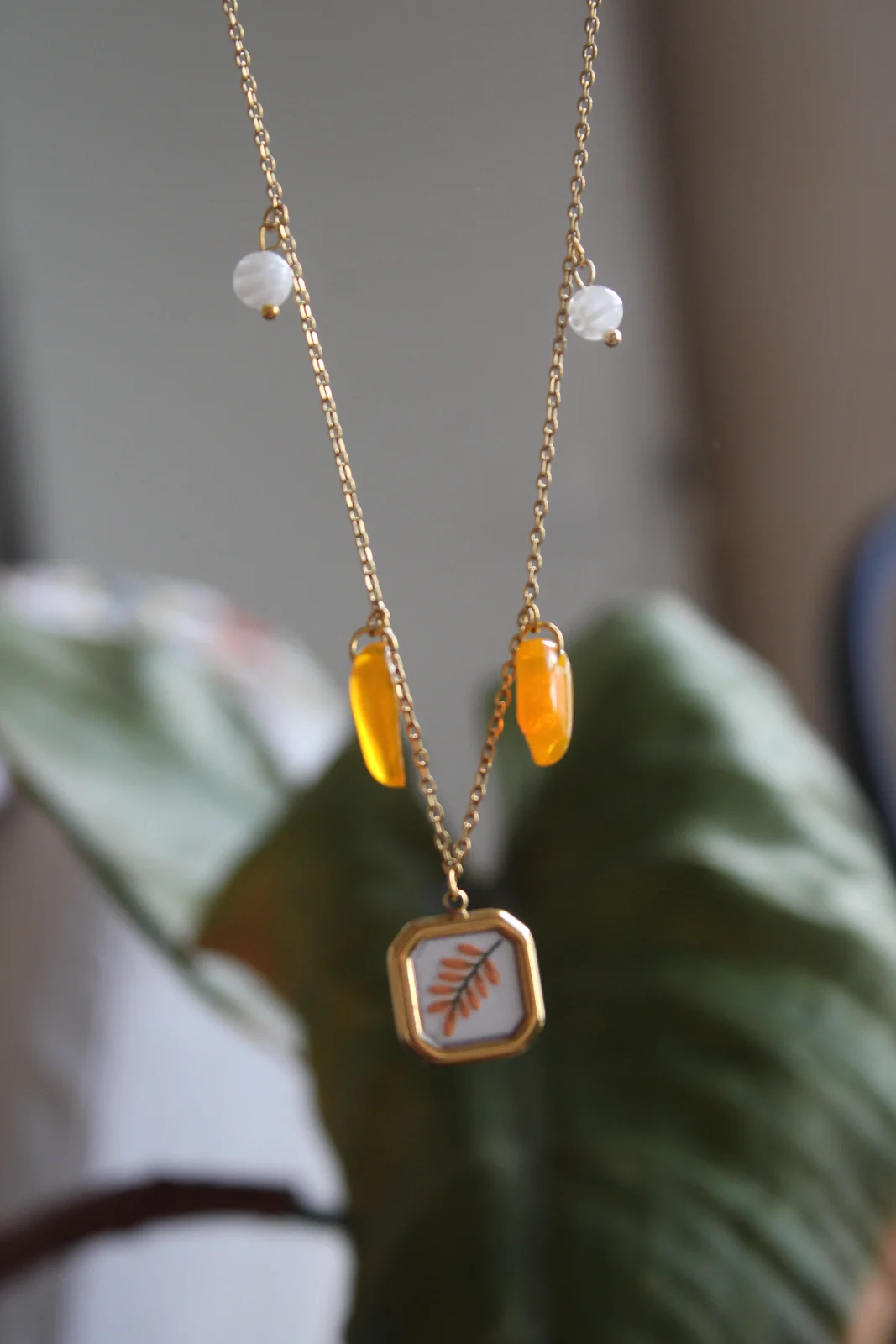 Gros plan du pendentif doré orné d'une feuille avec pampilles orange translucides et perles blanches