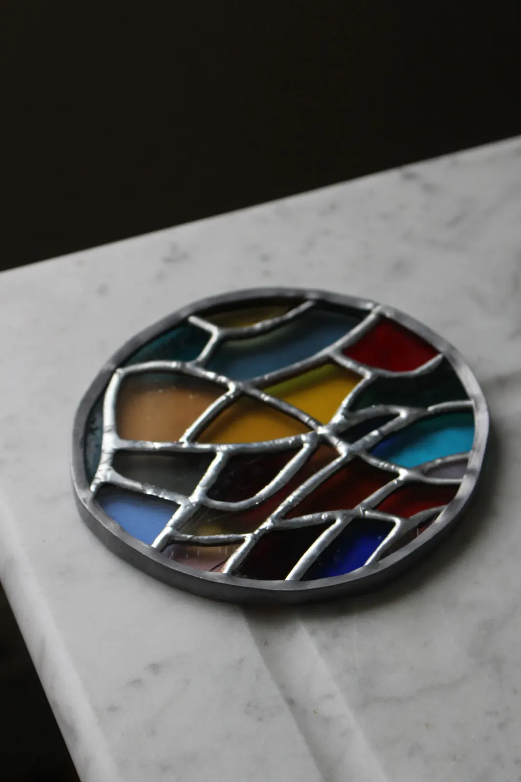 Vitrail circulaire aux formes géométriques et colorées posé à plat sur une surface en marbre.