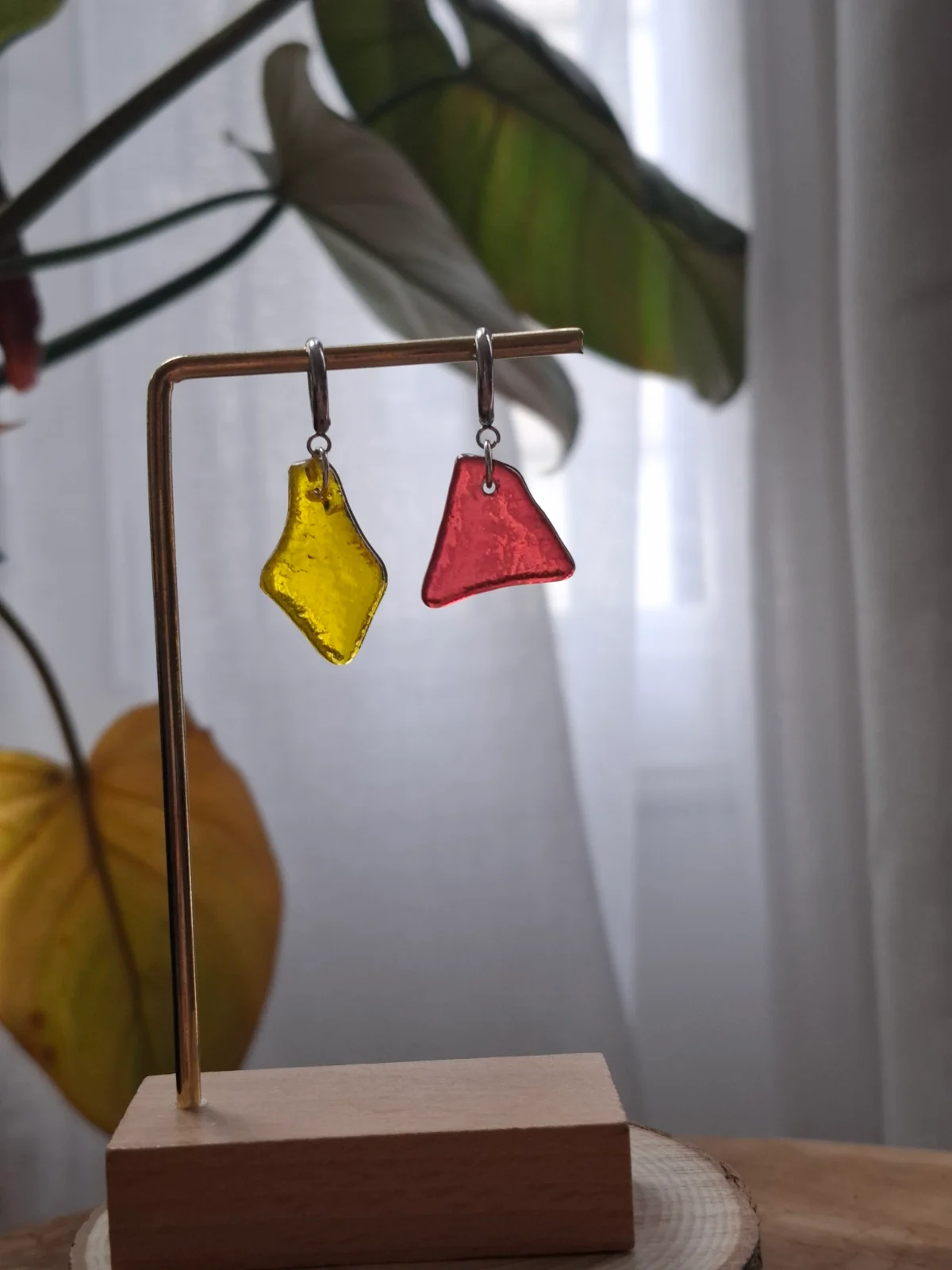 Paire de boucles pendantes en verre rouge et jaune suspendues à un présentoir en métal et bois.
