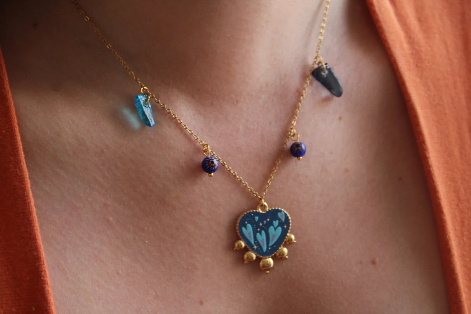 Collier fin doré porté au cou avec pendentif cœur bleu et pampilles asymétriques