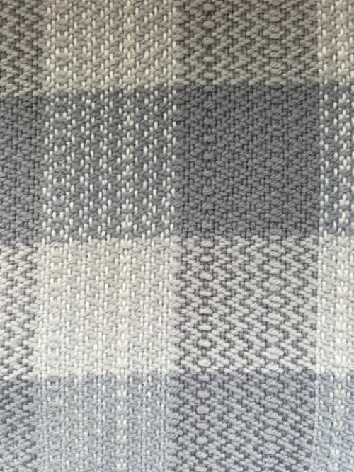 Détail rapproché du tissage artisanal aux motifs géométriques en laine blanche et grise.