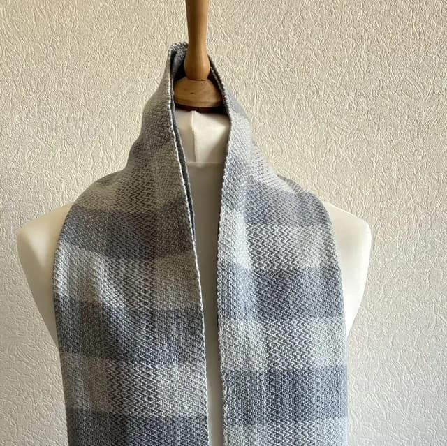 Écharpe tissée à motifs de carreaux blanc et gris, disposée sur un buste de mannequin.