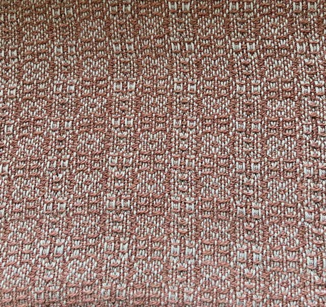 Gros plan sur le motif géométrique et la texture du tissage artisanal rose et écru.