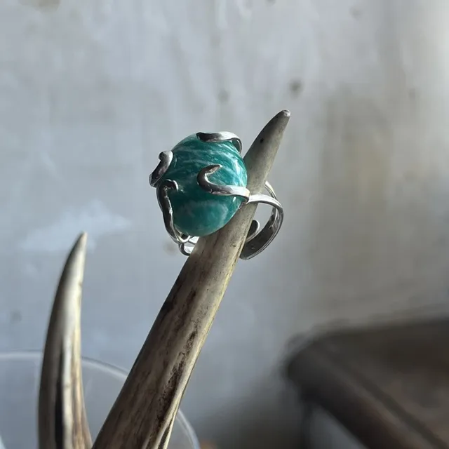 Bague sertie d'une amazonite turquoise portée au doigt sur fond végétal verdoyant