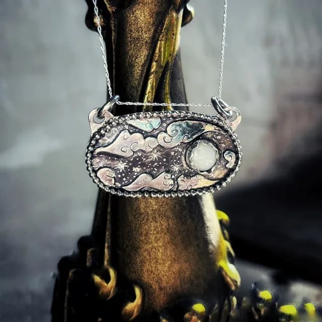 Collier en argent avec médaillon gravé motif nuages et lune d'opale porté au cou.