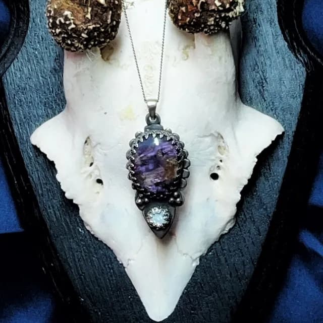 Gros plan sur le pendentif Éclipse en argent ciselé orné d'une charoite violette et d'une opale.