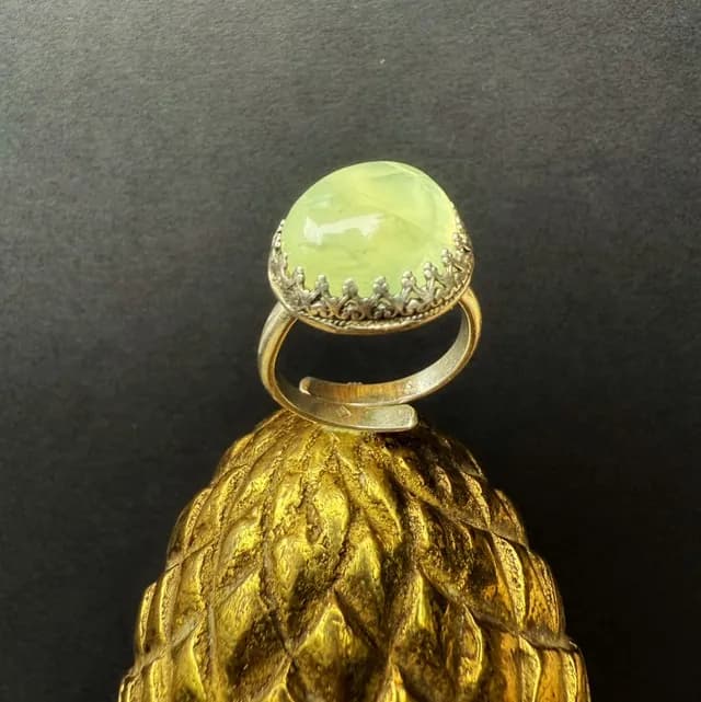 Bague argentée avec sertissage ouvragé et pierre cabochon verte bombée sur fond neutre