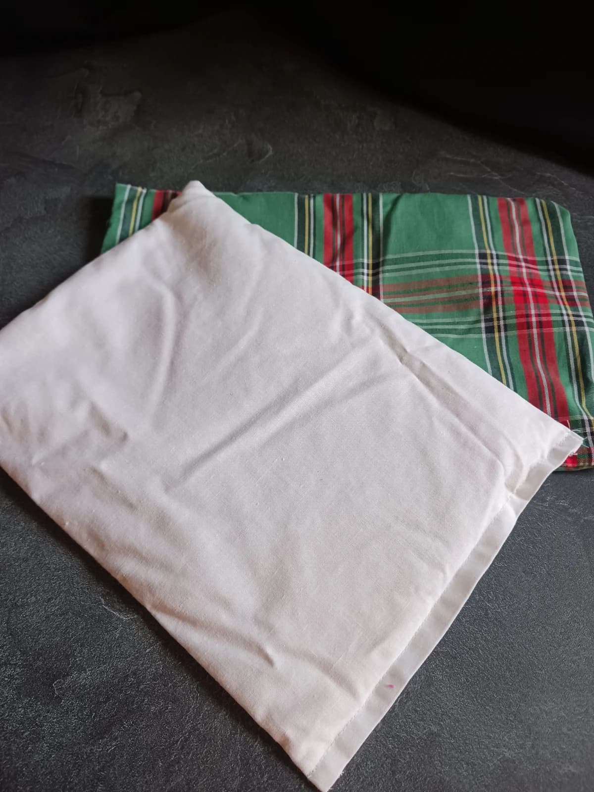 Pochette intérieure blanche posée sur la housse de coussin à motif tartan vert et rouge.
