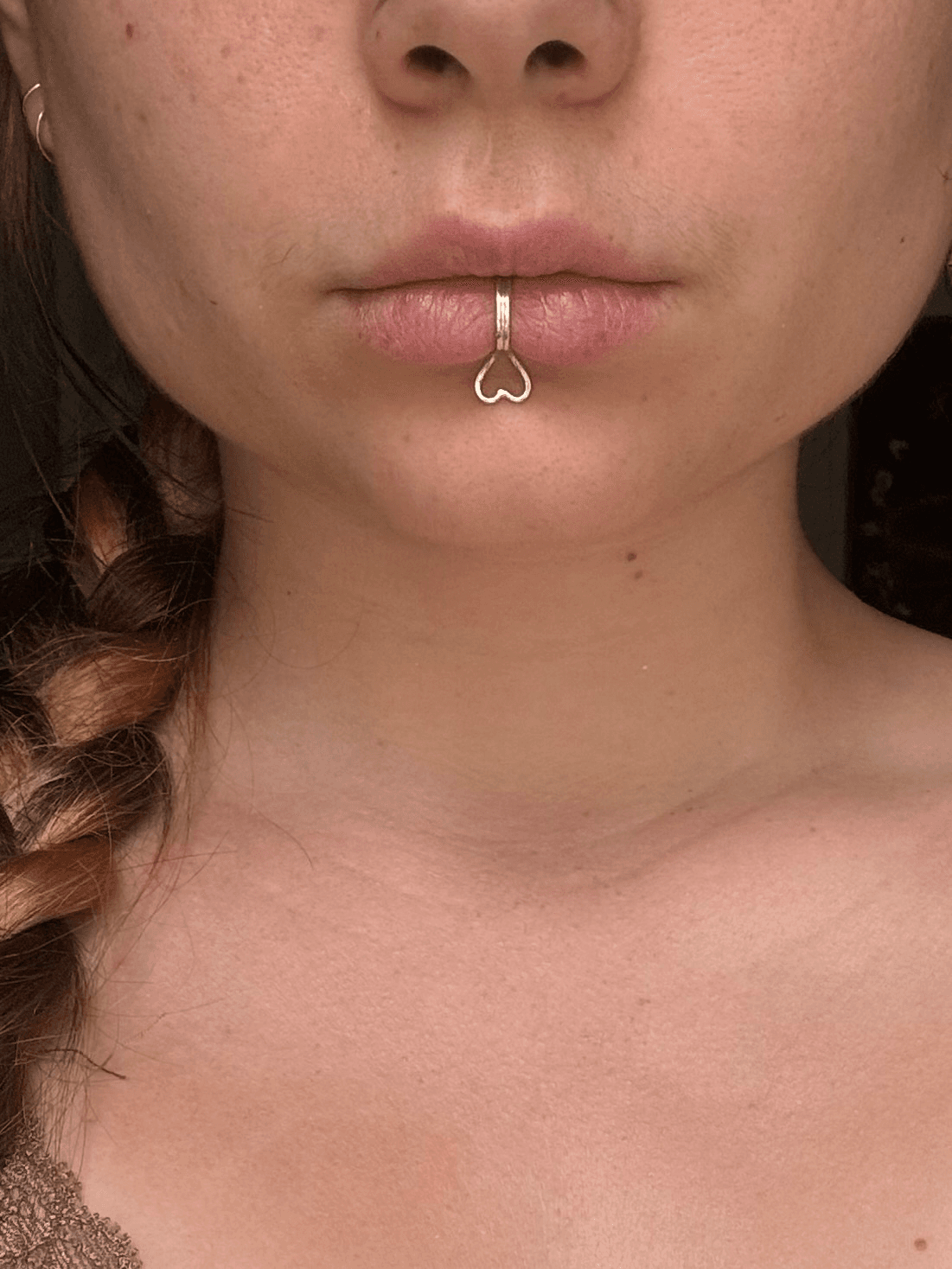 Bague de bouche argentée avec motif cœur portée au centre de la lèvre inférieure, vue de face.